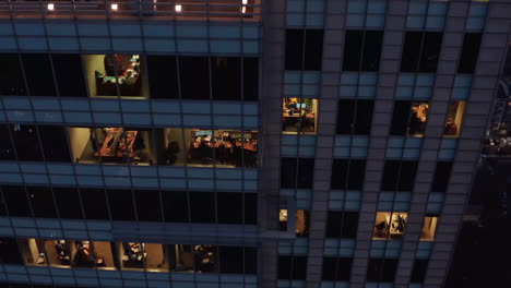 Rising-tilt-down-footage-of-lighted-windows-in-tall-business-building-in-city.-Evening-view-into-offices.-Warsaw,-Poland