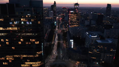 Aerial-evening-footage-of-heavy-traffic-in-city.-Tilt-up-reveal-of-downtown-skyscrapers-against-colourful-sunset-sky.-Warsaw,-Poland