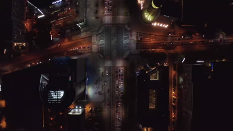 Aerial-birds-eye-overhead-top-down-view-of-traffic-in-night-city.-Cars-driving-through-intersection-and-others-directions-waiting-for-green-light.-Warsaw,-Poland