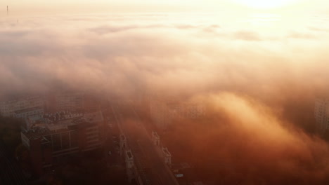Fly-above-morning-city.-Limited-visibility-due-to-fog-or-low-clouds-and-bright-rising-sun.-Warsaw,-Poland