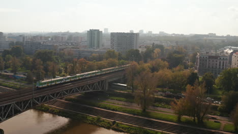 Tracking-of-suburban-train-riding-on-bridge-and-on-multitrack-line-through-town.-morning-view-of-transport-in-city.-Warsaw,-Poland
