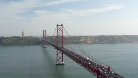 Elevated-view-of-long-red-cable-stayed-bridge-over-Tagus-river.-Multilane-road-with-heavy-traffic-from-drone.-Lisbon,-capital-of-Portugal.
