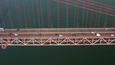 Seitenschieberansicht-Des-Geschäftigen-Mehrspurigen-Verkehrs-über-Eine-Rote-Brücke-über-Dem-Meer.-Autos-überqueren-Die-Hängebrücke-Ponte-25-De-Abril-In-Lissabon,-Portugal