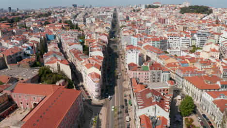 Aerial-drone-view-of-long-straight-street-in-city.-Camera-tilts-down-and-zooms-in-to-house-on-sharp-street-corner.-Lisbon,-capital-of-Portugal.