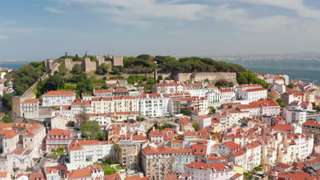 Aerial-view-of-Castelo-de-S-Jorge-Lisbon-castle-on-the-hill-above-colorful-traditional-houses-in-urban-city-center-of-Lisbon,-Portugal