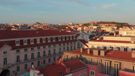 Elevated-evening-view-of-bright-sun-illuminated-buildings-downtown.-Drone-flying-over-red-rooftops.-Lisbon,-capital-of-Portugal.