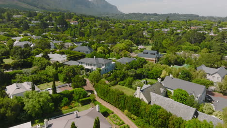 Houses-surrounded-by-lush-green-trees-and-shrubs.-Backwards-fly-above-residential-borough-with-family-houses.-Revealing-mountains-in-background.-Cape-Town,-South-Africa