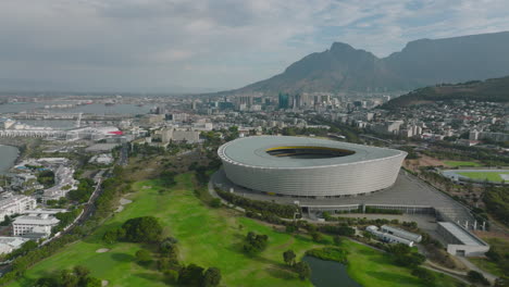 Forwards-fly-above-golf-course-at-Green-Point-Stadium.-Modern-football-arena-in-city.-Mountains-in-background.-Cape-Town,-South-Africa