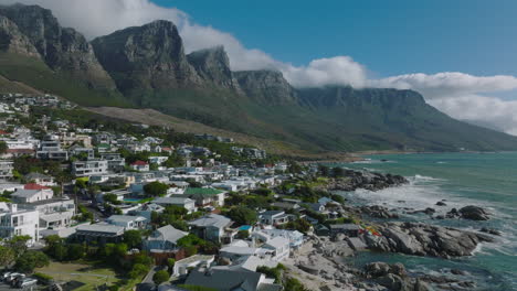 Forwards-fly-above-villas-and-luxury-residences-in-seaside-borough.-Beautiful-mountain-ridge-with-steep-rock-escarpments.-Cape-Town,-South-Africa