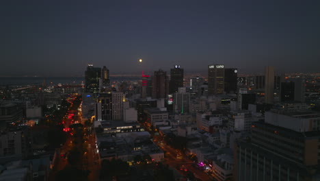 Rising-shot-of-city-centre-at-night.-Illuminated-streets-and-high-rise-buildings.-Revealing-sea-bay-with-seaport.-Cape-Town,-South-Africa