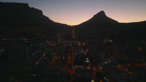 Romantic-shot-of-night-city-with-long-straight-streets-lit-by-street-lights-and-colourful-twilight-sky-with-mountain-silhouettes.-Cape-Town,-South-Africa