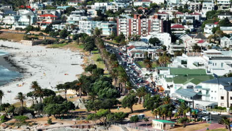 Summer-vacation-destination.-Buildings-in-tropical-tourist-resort-and-people-on-sand-beach-in-Camps-Bay.-Windy-weather-on-sunny-day.-Cape-Town,-South-Africa
