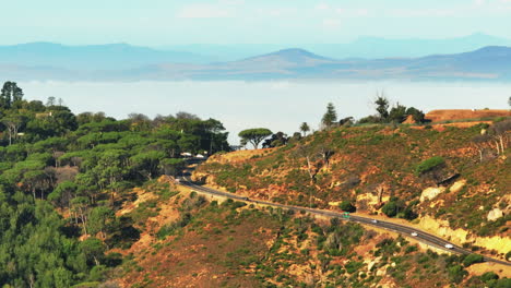 Slide-and-pan-footage-of-cars-passing-on-road-in-countryside.-Mountain-ridges-and-fog-flooded-valley-in-background.-Cape-Town,-South-Africa