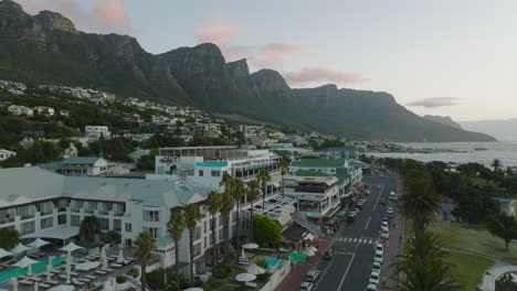 Fly-above-road-on-waterfront.-Vacation-resort-on-seaside-under-monumental-rocky-peaks.-Cape-Town,-South-Africa