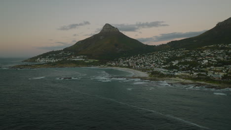 Panoramaaufnahme-Der-Meeresbucht-Mit-Sandstrand-Und-Gebäuden-Im-Stadtbezirk-In-Der-Dämmerung.-Kapstadt,-Süd-Afrika