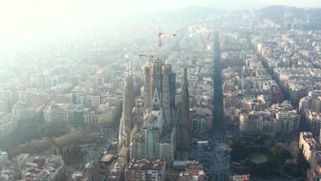 Forwards-fly-above-urban-borough.-Aerial-view-of-construction-site-of-large-church.-Famous-unfinished-basilica-Sagrada-Familia.-Barcelona,-Spain