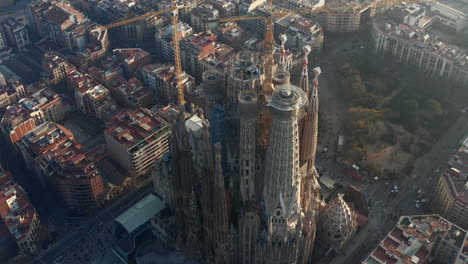 Fly-around-tall-tower-cranes-on-construction-site-of-unfinished-large-church.-Aerial-view-of-basilica-Sagrada-Familia.-Barcelona,-Spain