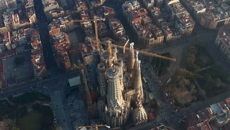 Aerial-footage-of-famous-unfinished-basilica-Sagrada-Familia-and-surrounding-buildings-at-golden-hour.-Barcelona,-Spain