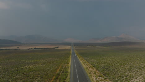 Forwards-fly-above-road-leading-straight-in-flat-landscape-with-mountains-in-distance.-Low-traffic-on-road.-South-Africa