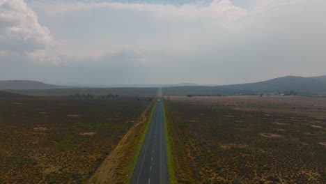Forwards-ascending-fly-above-barren-land.-Vehicles-sporadically-driving-on-straight-road-leading-over-horizon.-South-Africa
