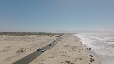 Sand-beach-on-ocean-coast-on-sunny-day-with-clear-sky.-Traffic-on-road-leading-along-shore.