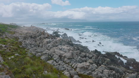 Group-of-tourists-climbing-on-rugged-coastal-rocks.-Orbit-shot-around-people-watching-waves-crashing-on-coast.