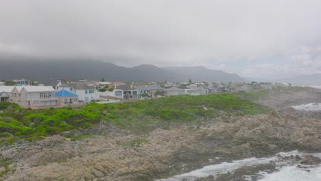 Family-houses-at-sea-cost.-Waves-washing-rugged-and-jagged-rocks.-Low-clouds-hiding-mountains-in-background.