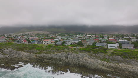 Pull-back-shot-of-people-standing-on-coastal-rocks-and-watching-crashing-waves.-Aerial-view-of-shore-near-Kleinmond.