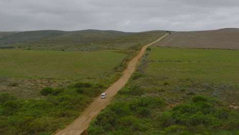 Forwards-tracking-of-big-passenger-car-driving-on-path-in-landscape.-Dirt-road-leading-between-agricultural-fields-with-green-vegetation.-South-Africa