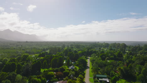 Adelante-Vuelo-Ascendente-Por-Encima-De-Desarrollo-Residencial-Esparcido-Entre-La-Vegetación-Verde.-Vista-Aérea-Contra-El-Sol.-Sudáfrica