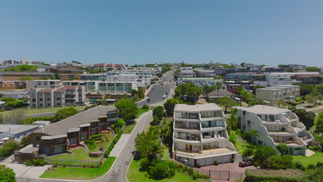 Apartment-houses-and-hotels-around-multilane-road-in-urban-borough.-Forwards-fly-above-town-development-on-sunny-day-with-clear-sky.-Plettenberg-Bay,-South-Africa