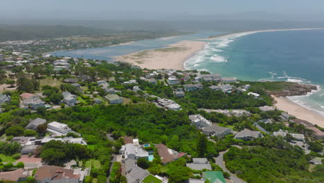 Aerial-view-of-luxury-houses-on-slope-with-green-vegetation-descending-to-sea-coast.-Plettenberg-Bay,-South-Africa