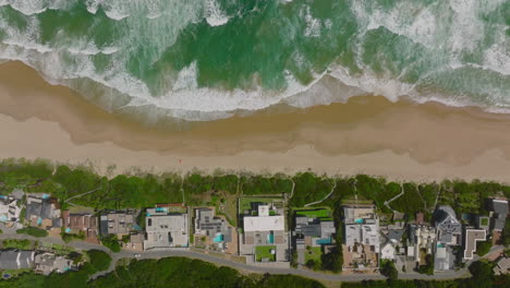 Top-down-panning-footage-on-buildings-along-sea-coast.-Amazing-shot-of-waves-rolling-to-sand-beach.-South-Africa