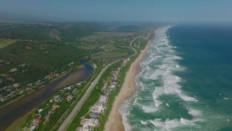 Erstaunliche-Panoramaaufnahmen-Aus-Der-Luft-Von-Der-Meeresküste-Mit-Rollenden-Wellen.-Straße-Und-Häuserzeile-Am-Sandstrand.-Südafrika