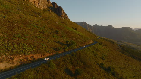 Tracking-of-cars-driving-on-road-winding-around-mountain-ridge-in-countryside.-Amazing-landscape-in-golden-hour.-South-Africa
