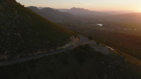 Luftpanoramaaufnahmen-Der-Landschaft-Bei-Sonnenuntergang.-Straße,-Die-Um-Den-Berg-Herumführt,-Hoch-über-Einem-Weiten-Tal.-Südafrika