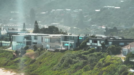 Slide-and-pan-footage-of-row-of-houses-elevated-above-sand-beach-leading-along-sea-coast.-South-Africa