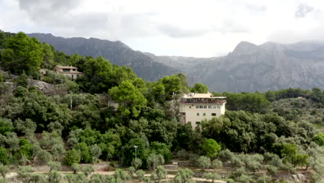 AERIAL:-House-in-Jungle-Mountains-on-Tropical-Island-Mallorca,-Spain-on-Sunny-Day-Vacation,-Travel,-Sunny,-Waves