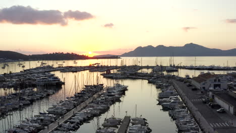 AERIAL:-Port-on-Tropical-Island-with-Sailboats-and-Ocean-at-Small-Town-at-Sunrise-with-Mountains-in-Background-Vacation,-Travel,-Sunset
