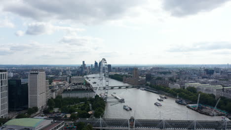 Crane-footage-of-wide-river-flowing-through-large-city.-Thames-river-at-Houses-of-Parliament-and-London-eye.-Short-tilt-down-shot-on-traffic-on-Waterloo-Bridge.-London,-UK