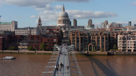 People-walking-on-Millennium-footbridge-over-River-Thames.-Forwards-fly-towards-Saint-Pauls-Cathedral-with-large-dome.-London,-UK