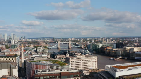 Slide-and-pan-footage-of-cityscape.-Panoramic-aerial-view-of-town-with-famous-Tower-Bridge-across-River-Thames.-Buildings-lit-by-bright-afternoon-sun.-London,-UK
