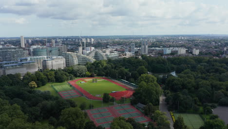 Slide-and-pan-footage-of-Millennium-Arena-and-tennis-courts-in-Battersea-Park-at-Thames-river.-Panoramic-view-of-city.-London,-UK