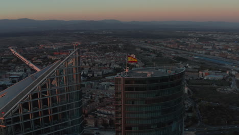 Aerial-shot-of-tops-of-skyscrapers-in-CTBA-business-hub.-Spanish-flag-on-rooftop.-City-at-dusk-in-background.