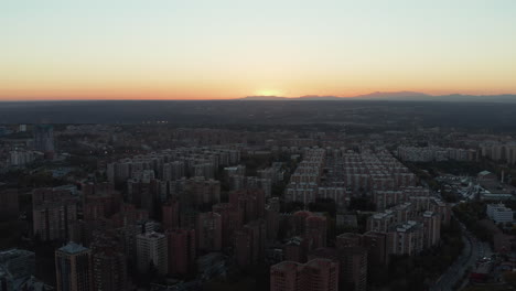 Aerial-view-of-apartment-houses-on-vast-housing-estate-in-town-at-dusk.-Sun-setting-behind-mountain-ridge-in-distance.