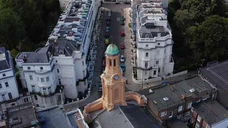 Descending-closeup-view-of-church-clock-tower.-Tilt-up-revealing-street-with-white-houses.-London,-UK
