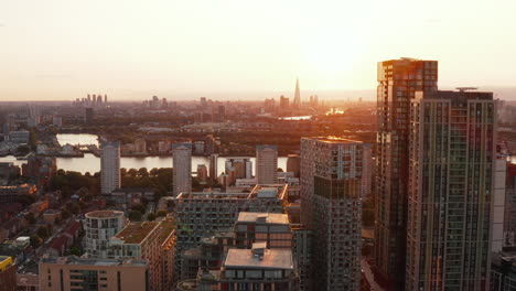 Forwards-reveal-of-buildings-in-Canary-Wharf-district.-Panoramic-aerial-view-of-cityscape-against-setting-sun.-London,-UK