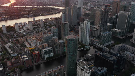 Tilt-and-pan-footage-of-modern-business-district-with-futuristic-buildings-around-water-channel.-Aerial-view-of-Canary-Wharf-in-sunset-time.-London,-UK
