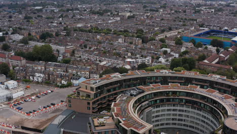 Backwards-reveal-of-round-ring-Television-centre-building-and-rows-on-family-houses-in-urban-neighbourhood.-London,-UK