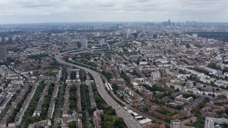Aerial-panoramic-view-of-multilane-highway-winding-through-urban-neighbourhood.-Skyline-with-modern-skyscrapers-in-background.-London,-UK